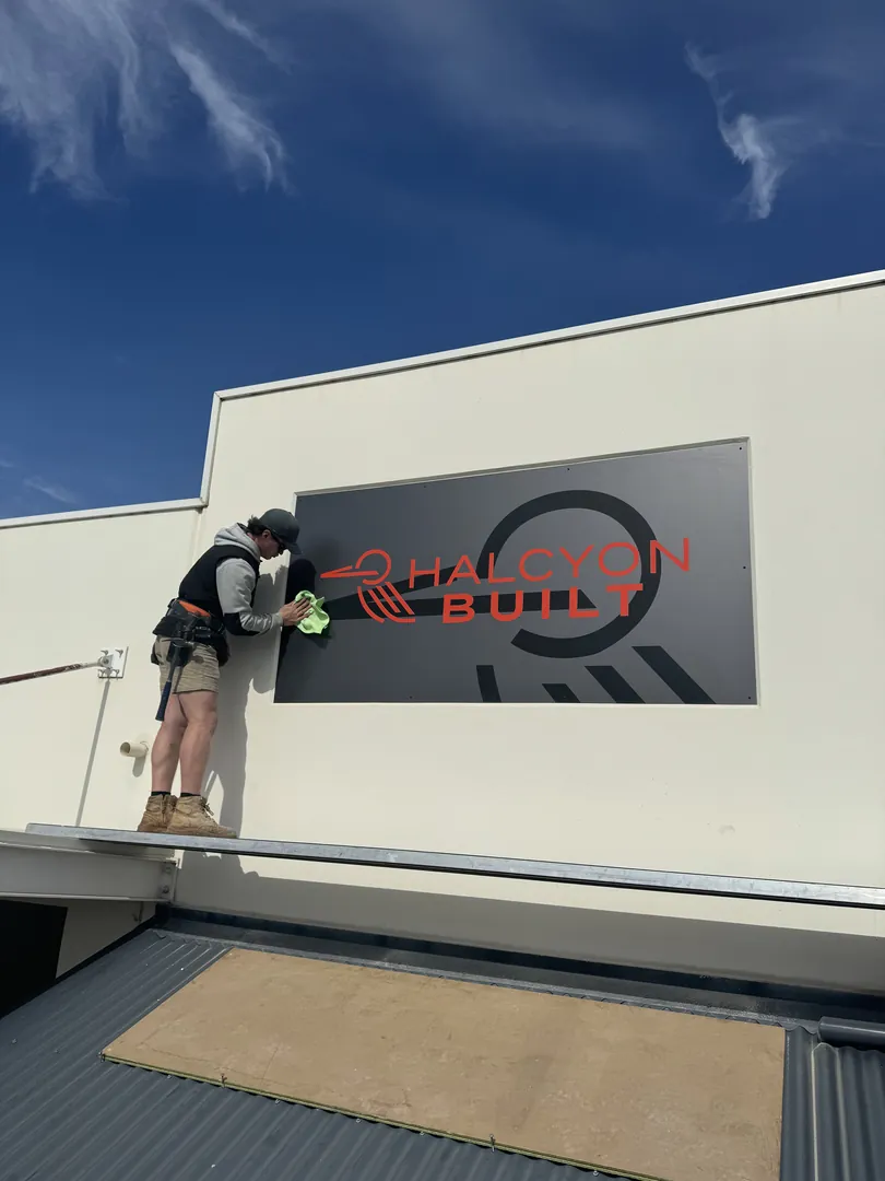 Worker cleaning Halcyon Built building sign.